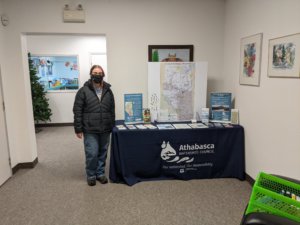 A woman is standing next to a table. The table has a map of the Athabasca Watershed as well as brochures.