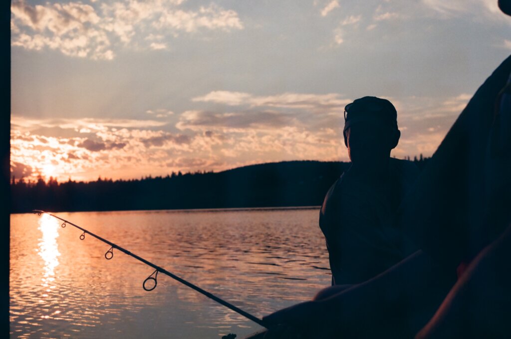A photo of a person and a fishing rod silhouetted against a sunset 